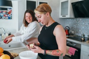 Two smiling females cooking a dinner in the kitchen. Same sex marriage couple in the home interior. Woman's health, happy pregnancy doula supporting and calm mental mood concept image.
