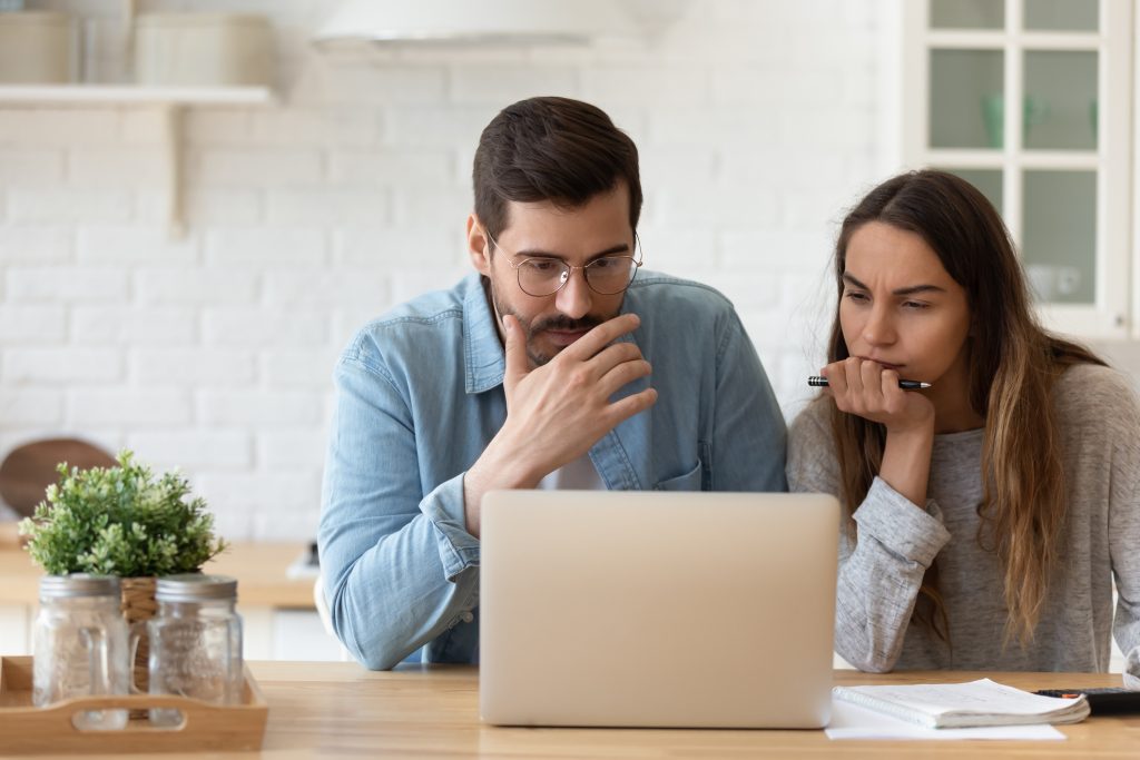 Serious concerned couple sit indoor looking at laptop